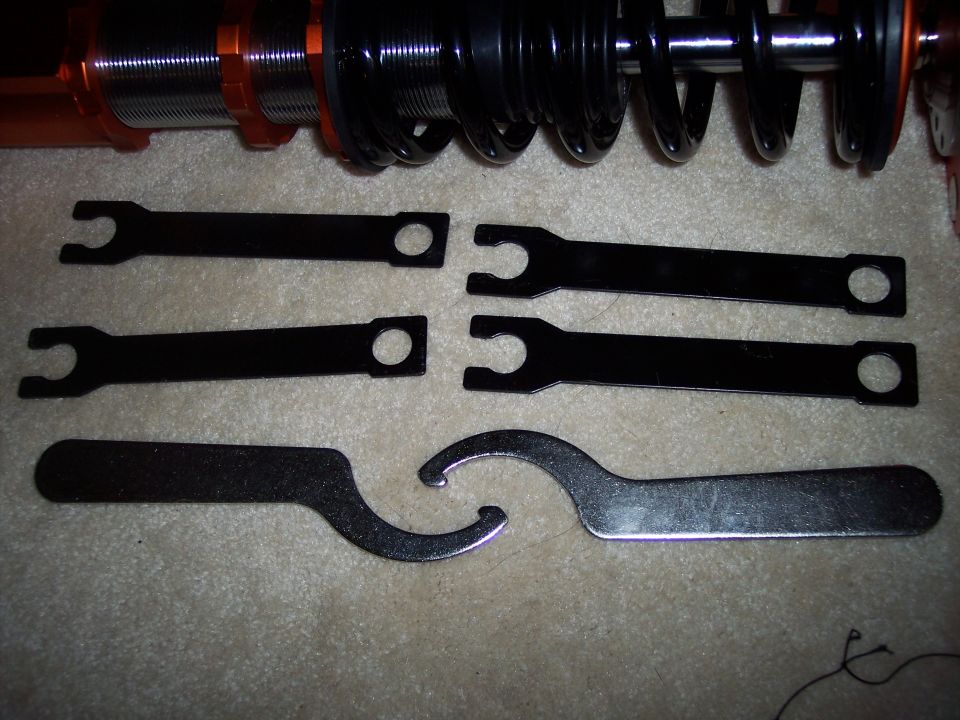 Adjustable coilover suspension parts with wrenches. Includes two coilover units and six adjustment wrenches