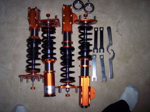 1995 Ford Probe - A set of four orange coilover suspension units and adjustment wrenches are laid out on a carpeted surface.