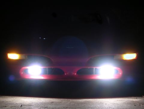 1996 Ford Probe - The front of a red car is illuminated by its headlights and turn signals in the dark.