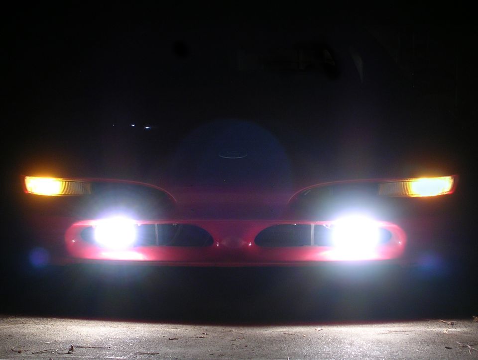 Red coupe at night with amber corner lamps and blazing white HID fog lights