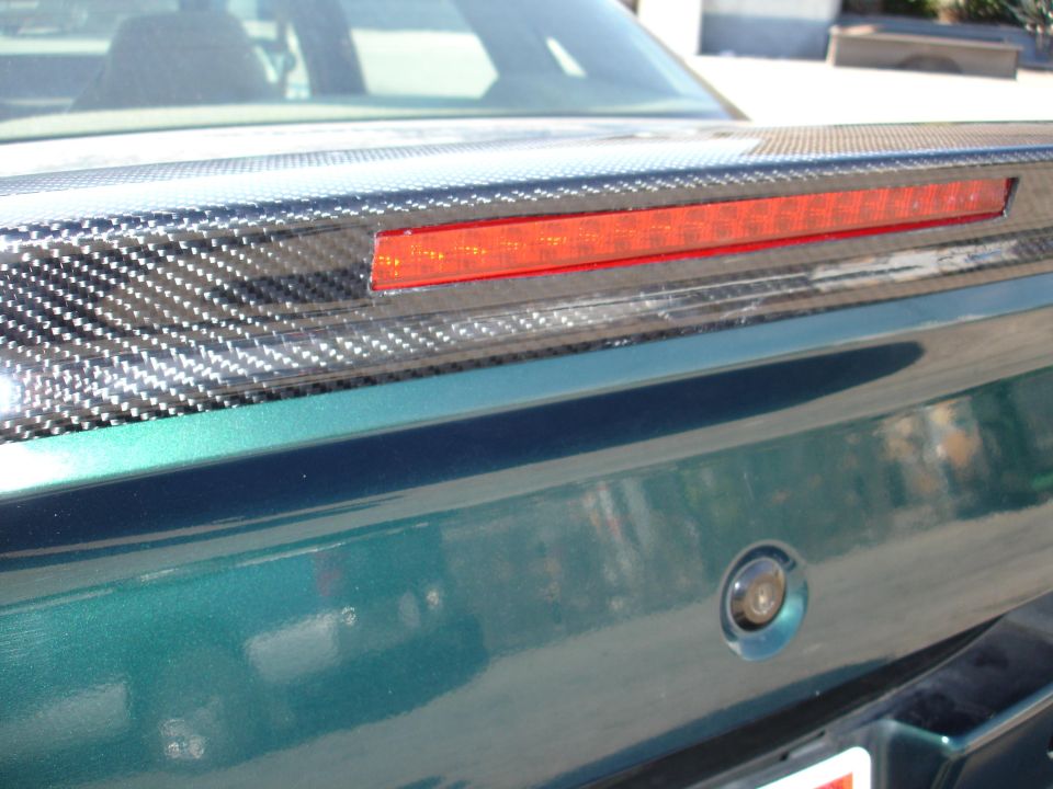 Rear spoiler with carbon fiber accents and red brake light on green car