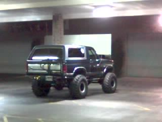 1985 Ford Bronco - This lifted Ford Bronco is parked indoors, possibly in a garage or parking structure.