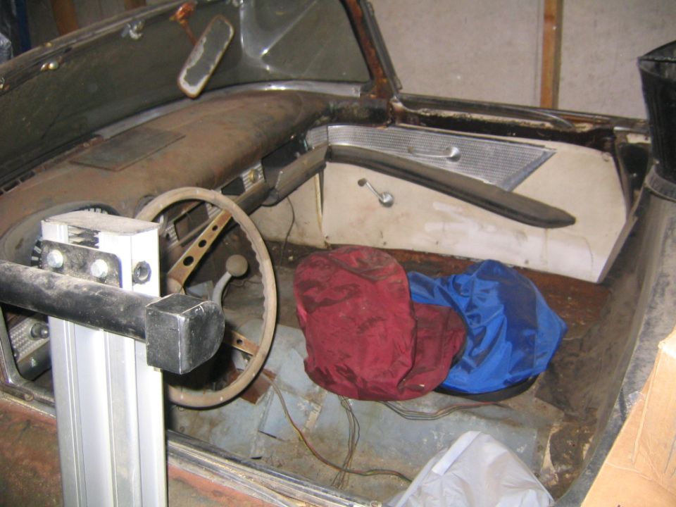 Stripped 1950s convertible interior with ivory steering wheel, bare rusty floor pan and loose wiring