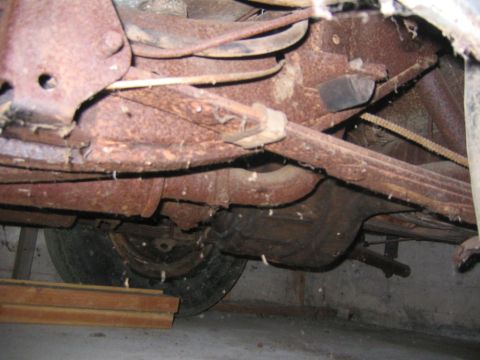 1956 Ford Thunderbird - The undercarriage of a heavily rusted vehicle is visible, showing suspension components and a tire.