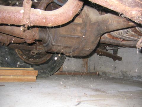 1956 Ford Thunderbird - Underside view of a vehicle's rear axle and suspension system, showing rusty components and a tire.