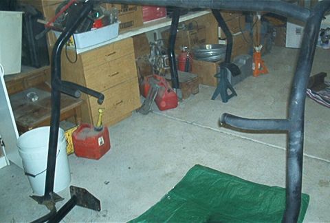 1986 Ford Bronco - A black roll cage is visible in a garage setting, surrounded by various tools and gas cans.