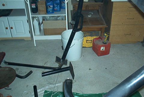 1986 Ford Bronco - Automotive parts including an exhaust pipe and jack stand are on a garage floor.