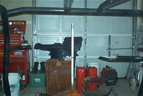 1986 Ford Bronco - A collection of items, including a roll cage, are stored in a garage in front of a closed overhead door.