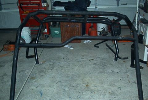 1986 Ford Bronco - A black metal roll cage is shown in a garage setting, with various tools and equipment in the background.