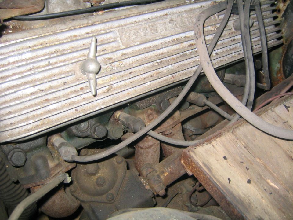 Close-up of an engine's aluminum valve cover with a metal cap and spark plug wires