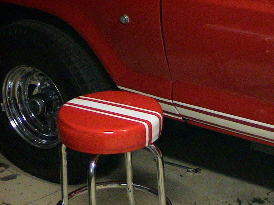 red vehicle side with racing stripes and a stool in front of it