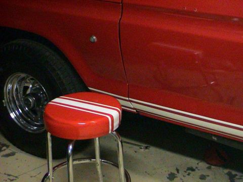 1979 Ford Bronco - A red vehicle's side panel and wheel are visible next to a stool.