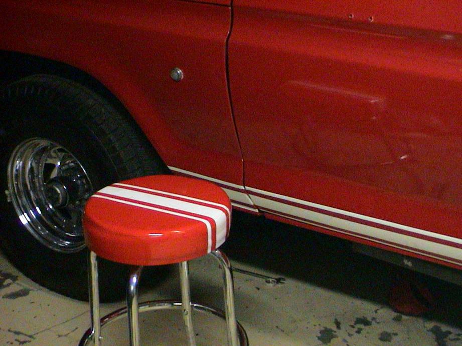 Red vehicle side with a white stripe, chrome wheel, and a red stool with white stripes