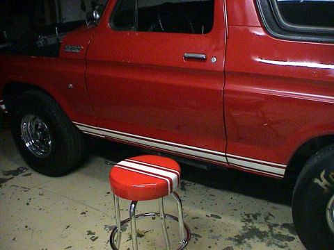 1979 Ford Bronco - Side profile of a red 1979 Ford Bronco a white racing stripe along the lower body.