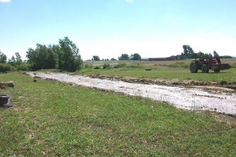 1979 Ford F-150 - Tractor with front loader in a muddy field with a dirt track and farm buildings in the background.