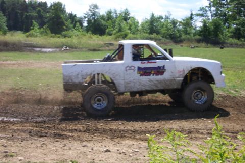 1979 Ford F-150 - A modified pickup truck navigates a muddy track, kicking up dirt as it goes.
