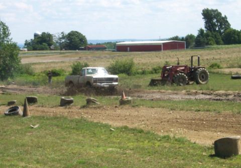 1979 Ford F-150 - A white 1979 Ford F-150 navigates a muddy track, with a tractor visible in the background on a sunny day.
