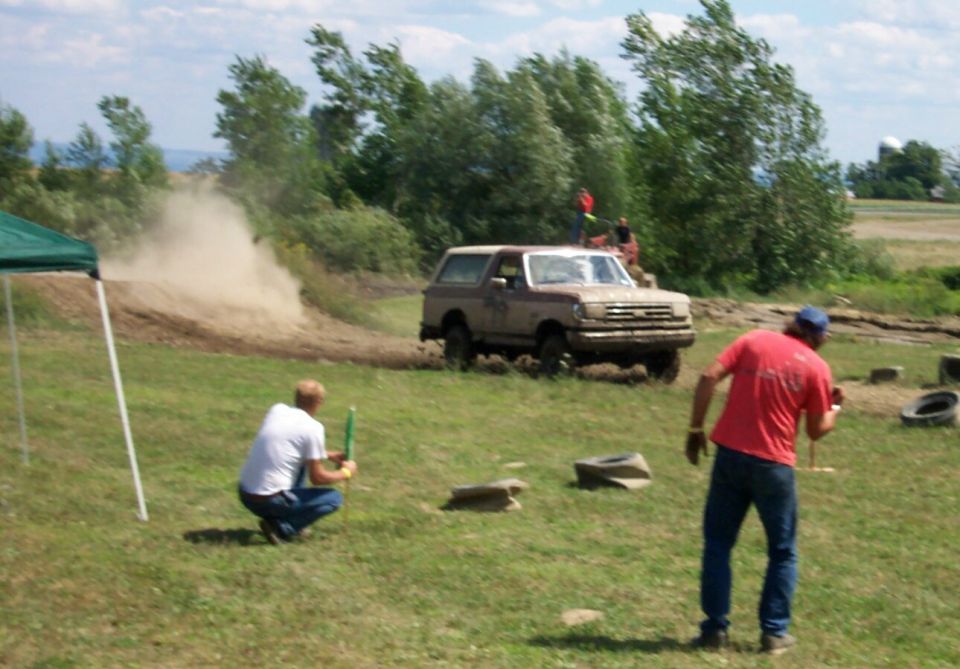 Muddy Ford Bronco kicking up dust on a dirt track with people watching