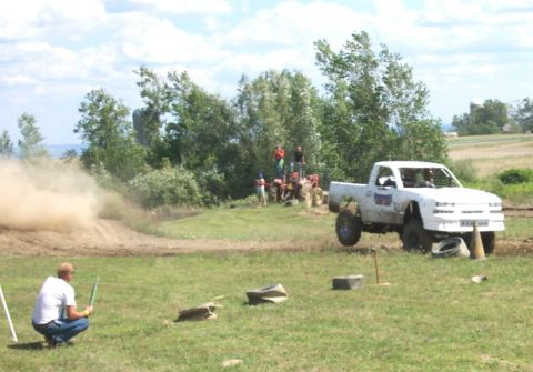 1979 Ford F-150 - A white pickup truck navigates a muddy course, with a tractor and spectators in the background.