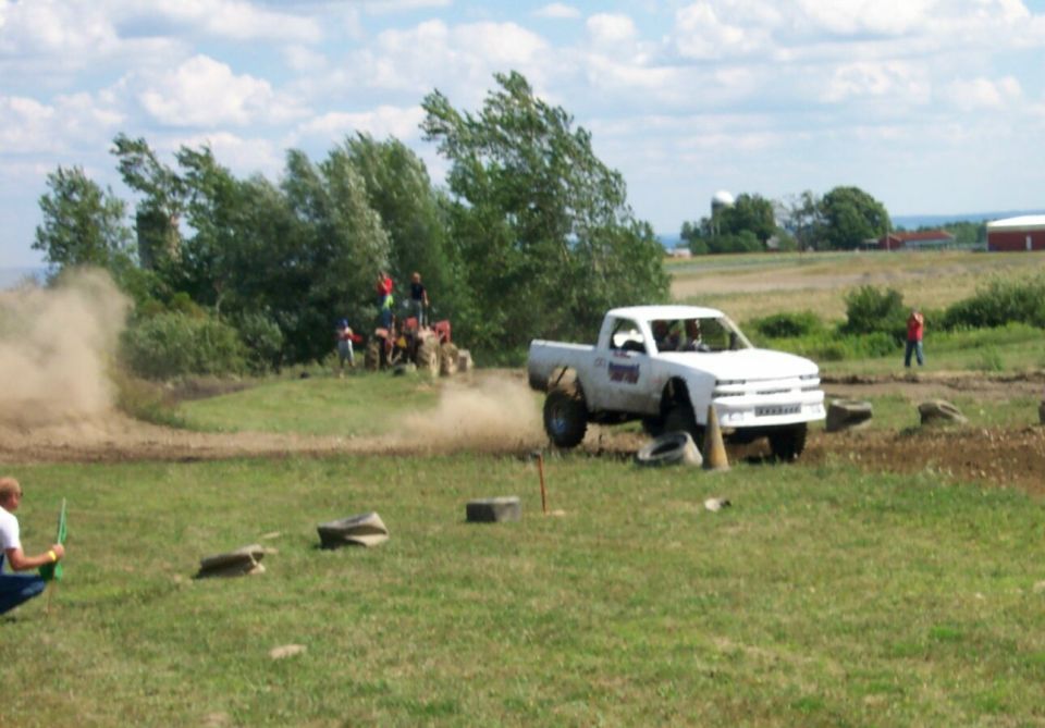White pickup truck with large tires navigating an off-road course, kicking up dust