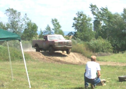 1979 Ford F-150 - A red 1979 Ford F-150 navigates a dusty dirt hill during an outdoor event.