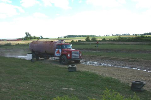 1979 Ford F-150 - A red tanker truck with a CITGO logo drives through a muddy field, kicking up water.