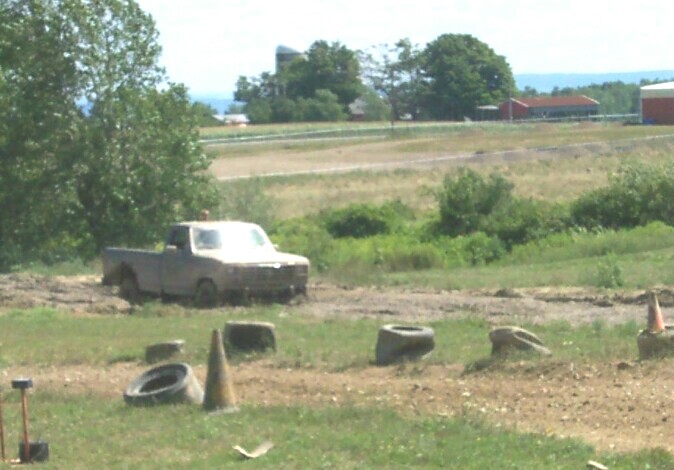 Mud-covered pickup truck in a field with tires and cones