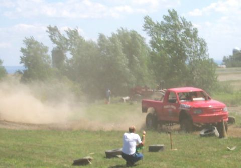 1979 Ford F-150 - A red pickup truck with a roll cage is seen on a grassy field, kicking up dust.