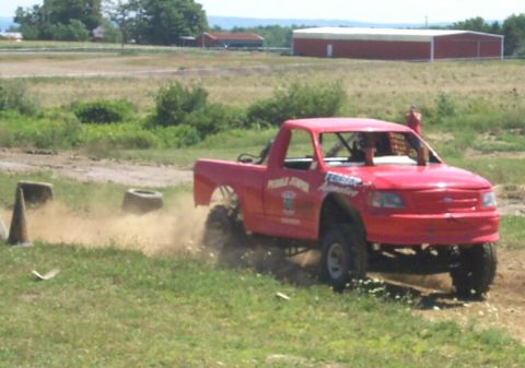 1979 Ford F-150 - A modified red pickup truck navigates an obstacle course, kicking up dust as it goes.