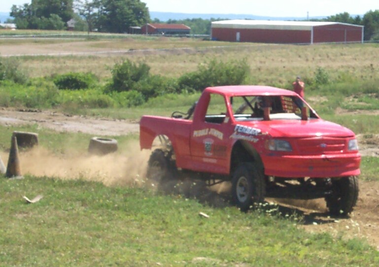 Red pickup truck with racing decals kicking up dirt