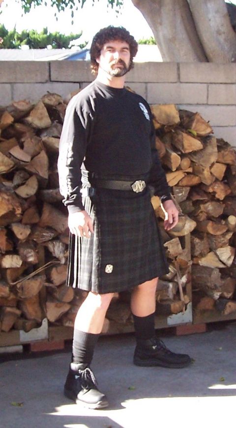 1990 Ford Bronco - A man wearing a kilt and black long-sleeved shirt stands outdoors in front of a wall of firewood.
