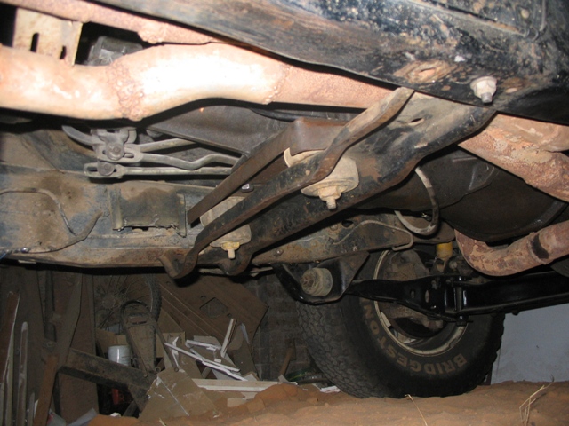 Underside of a vehicle with visible suspension components, exhaust pipes, and a tire with "BRIDGESTONE" text