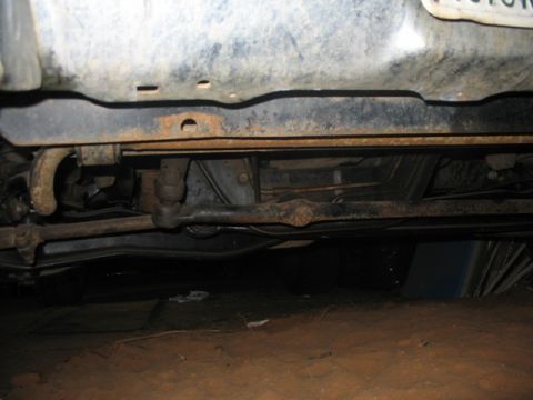 1981 Ford Bronco - The undercarriage of a vehicle shows its steering linkage and suspension parts, with some signs of wear and tear.