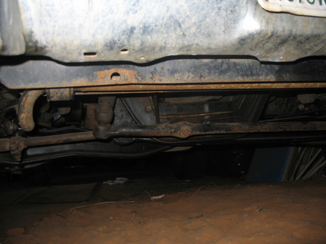 Underside view of a vehicle's steering and suspension components. Some rust is visible on the frame