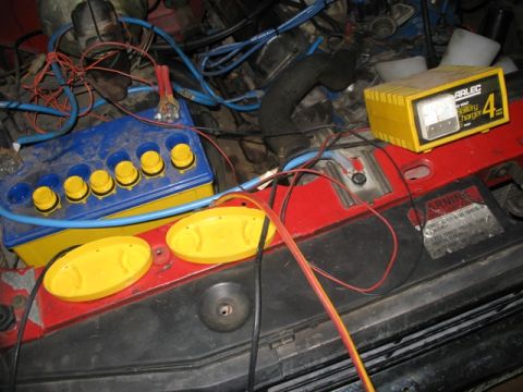 1981 Ford Bronco - A close-up view of a vehicle's engine bay shows a battery and a connected charger with jumper cables.