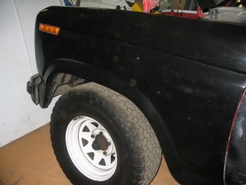 1981 Ford Bronco - Close-up of a black SUV's front fender and wheel, showing signs of wear and tear.