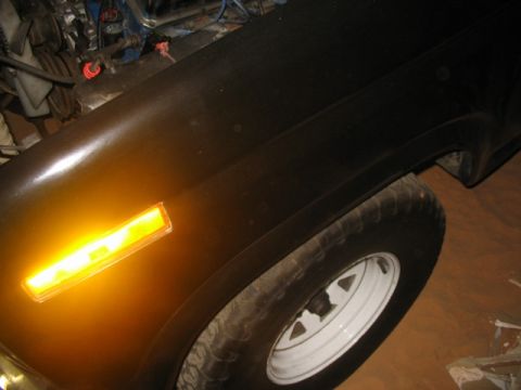 1981 Ford Bronco - Close-up view of a black vehicle's front fender, showing an amber turn signal and a white-rimmed wheel.