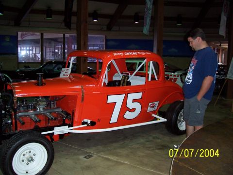 1987 Ford Bronco - A vintage race car with a roll cage and exposed engine is displayed indoors.