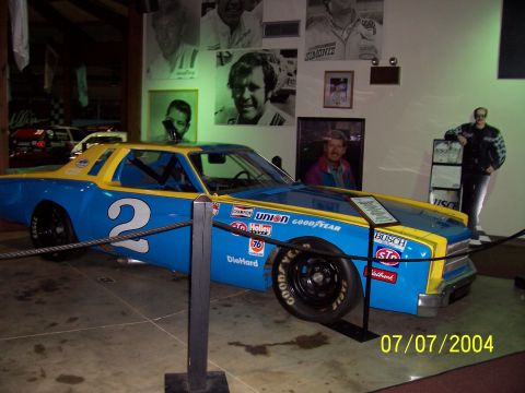 1987 Ford Bronco - A blue and yellow race car, number 2, is displayed indoors with portraits of drivers on the wall.