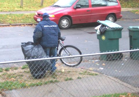1979 Ford F-150 - A man carries a large garbage bag while standing next to a bicycle and trash cans on a street.