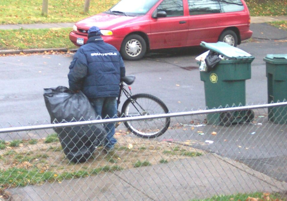 guy with garbage bag and bike next to trash cans, red van in background