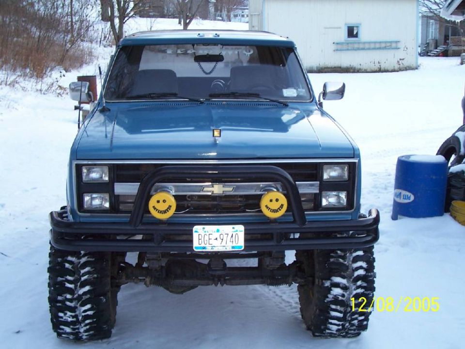 Blue pickup truck with a brush guard and smiley face fog lights in the snow