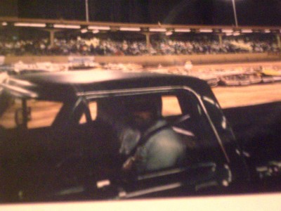 1972 Ford Ranchero - Interior view of a dark-colored vehicle with occupants, set against a backdrop of a stadium and race track.