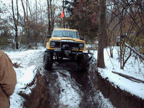 1977 Ford F-150 - A modified Jeep navigates a challenging off-road trail covered in snow and mud.