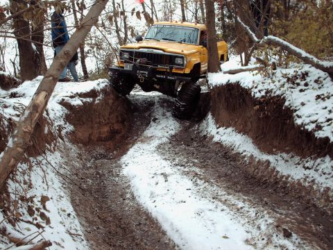 1977 Ford F-150 - A yellow Jeep truck tackles a challenging off-road course covered in snow and mud.