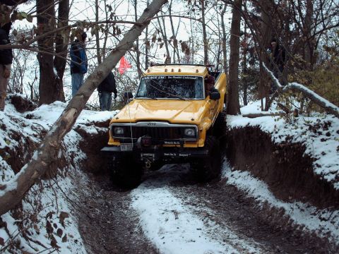 1977 Ford F-150 - This Jeep pickup truck navigates a challenging off-road trail covered in snow and mud.