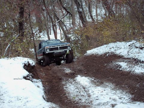 1977 Ford F-150 - A 1977 Ford F-150 navigates a challenging off-road trail with snow and mud.