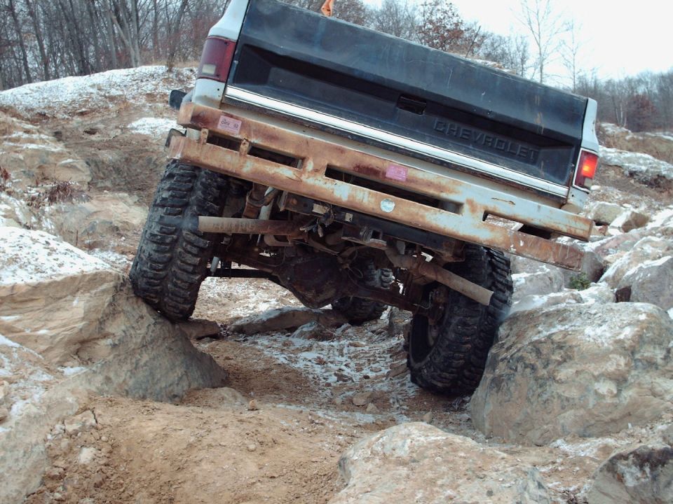 Black and white Chevrolet pickup truck with rusty bumper navigating rocks