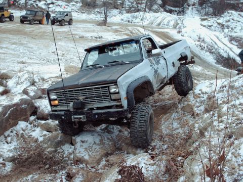 1977 Ford F-150 - A lifted pickup truck tackles a challenging off-road course with snow and rocks.