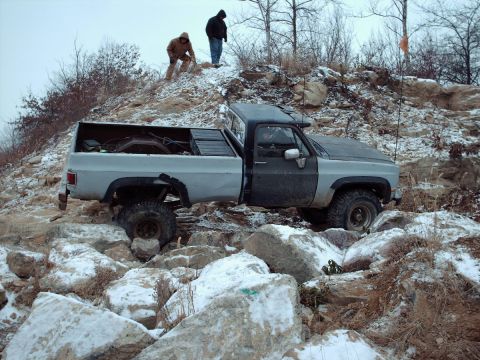 1977 Ford F-150 - A modified pickup truck is being driven over a challenging, rocky obstacle course in snowy conditions.